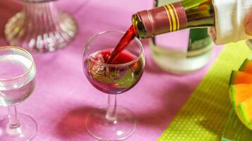 A bottle of red liquid being poured into a glass on a pink tablecloth.