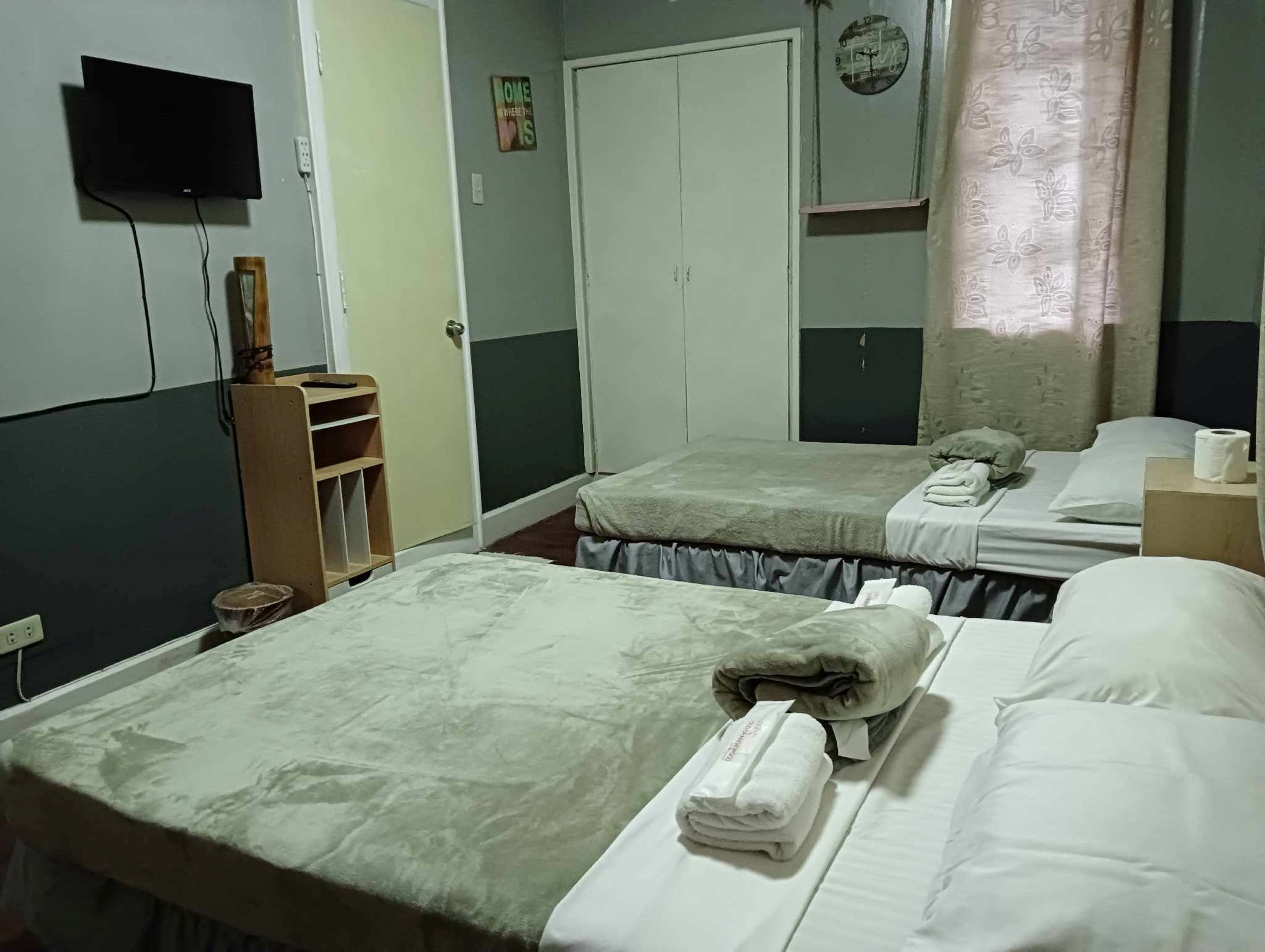 Een hotelkamer met twee bedden, een televisie, een kledingkast en een klok aan de muur.