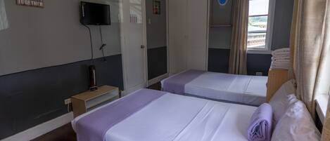 A room with two beds, a television, a wardrobe, and a window with curtains.