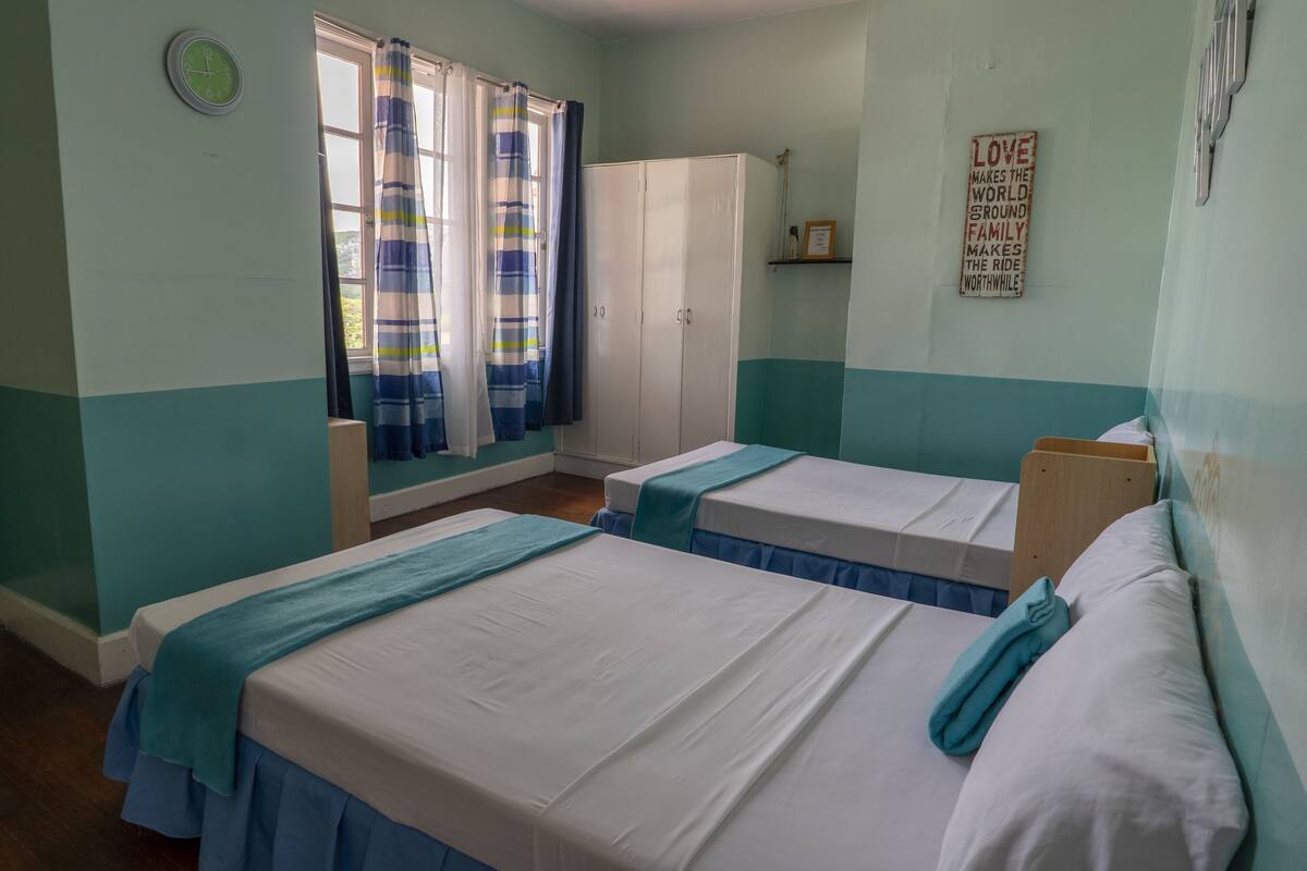 A room with two single beds, a wardrobe, a window with curtains, and a motivational quote on the wall.