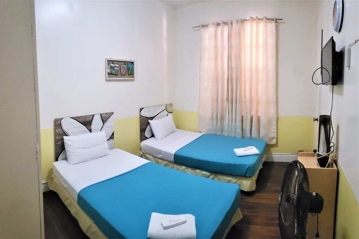 Une chambre d’hôtel avec deux lits, une télévision, un ventilateur et un rideau.