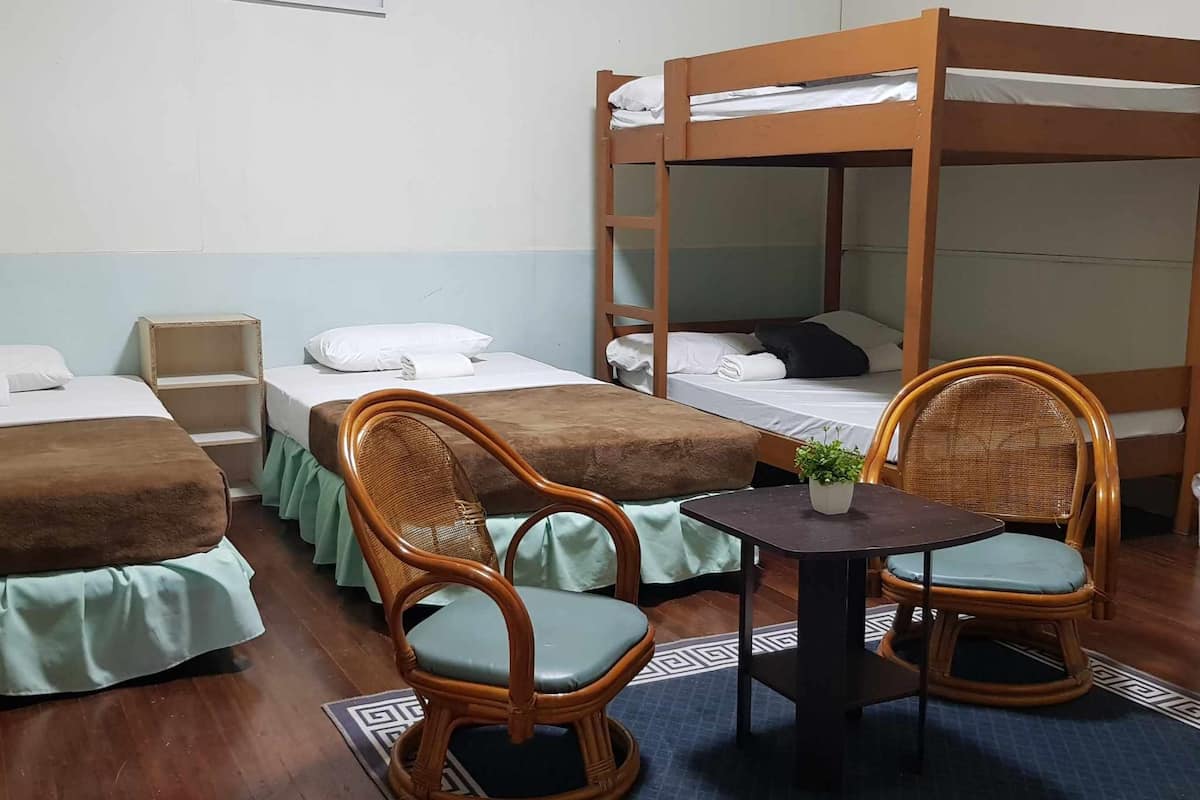 A room with bunk beds, two wicker chairs, a small table with a plant, and a patterned rug.