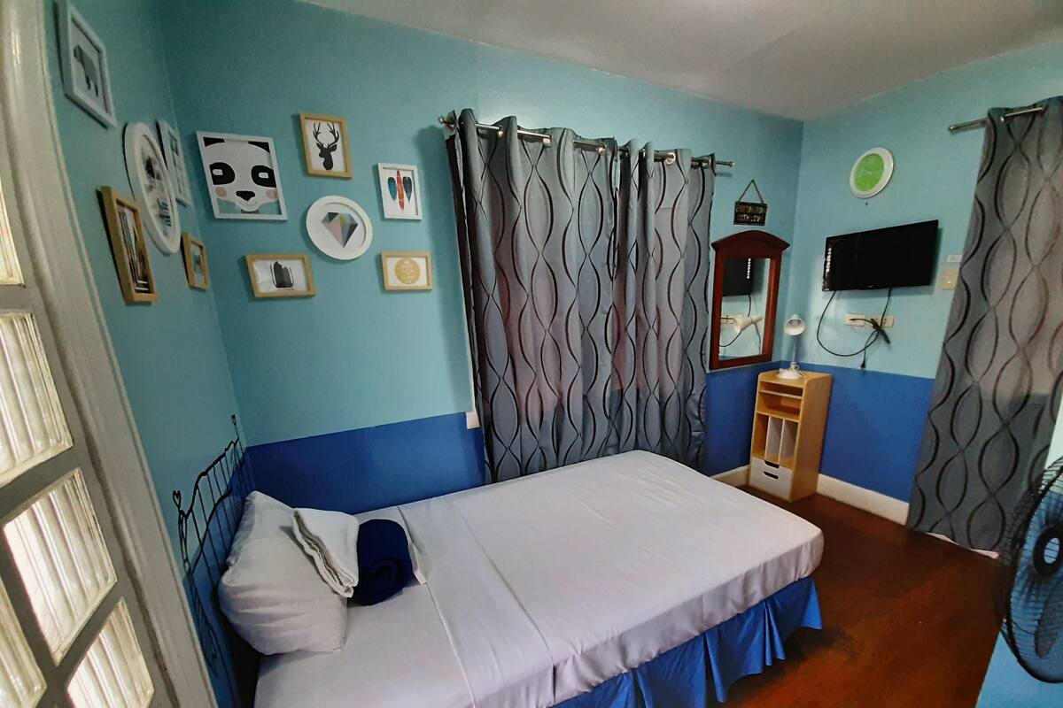 A bedroom with a bed, curtains, a mirror, a television, and wall decorations.
