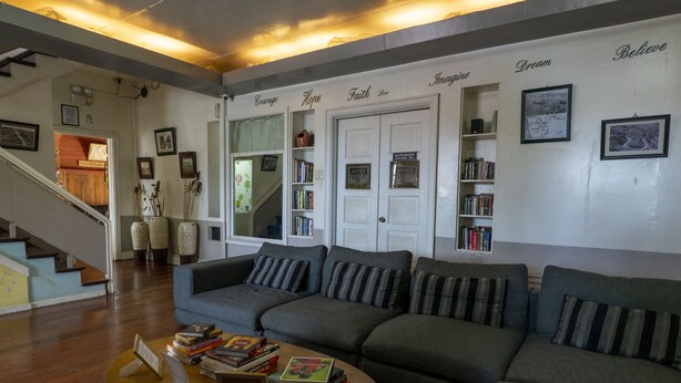 Una sala de estar con un sofá gris, una mesa de centro de madera con libros, una escalera y una estantería con cuadros y libros.