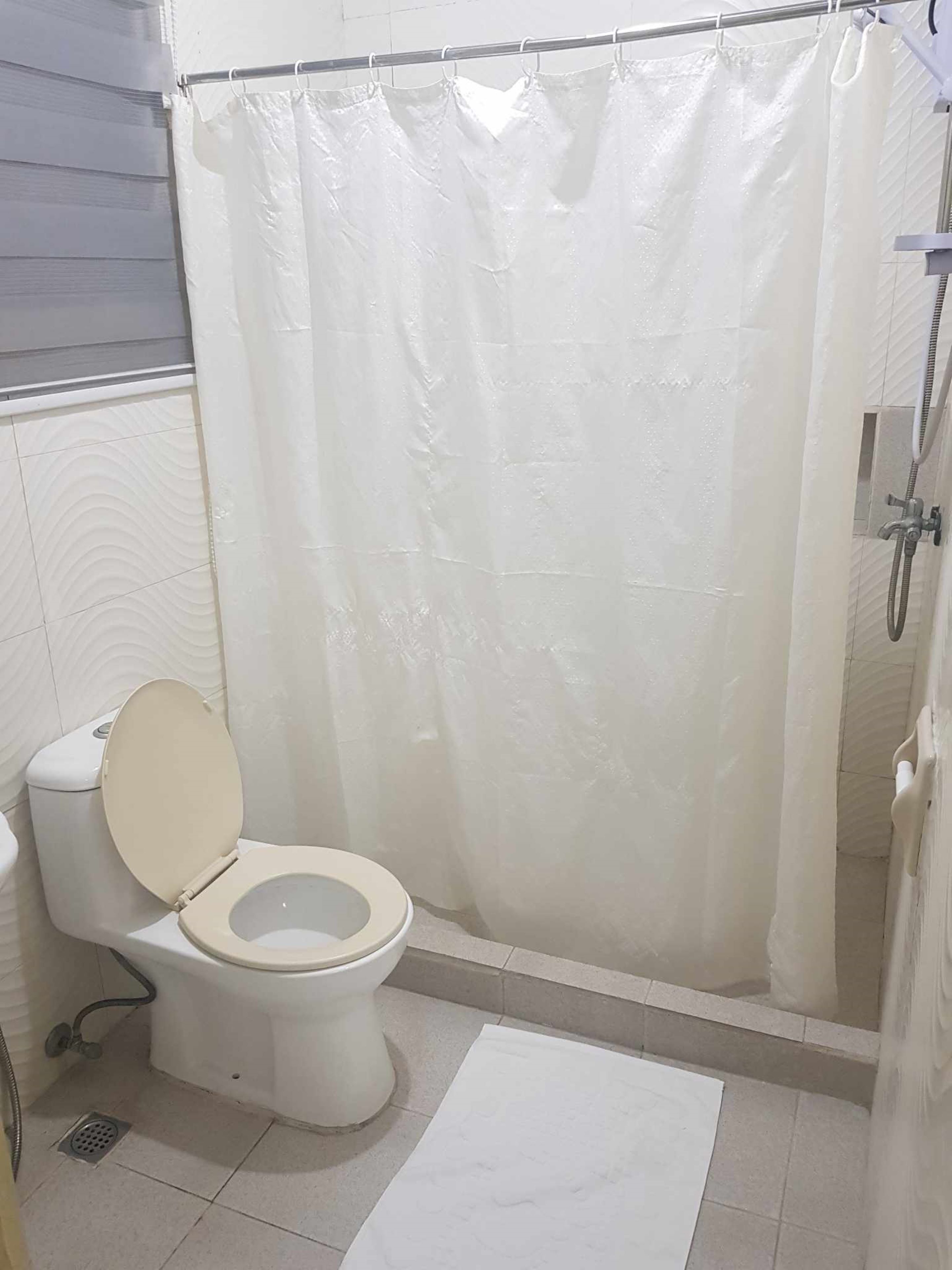 Un baño con inodoro, ducha y cortina de ducha blanca.