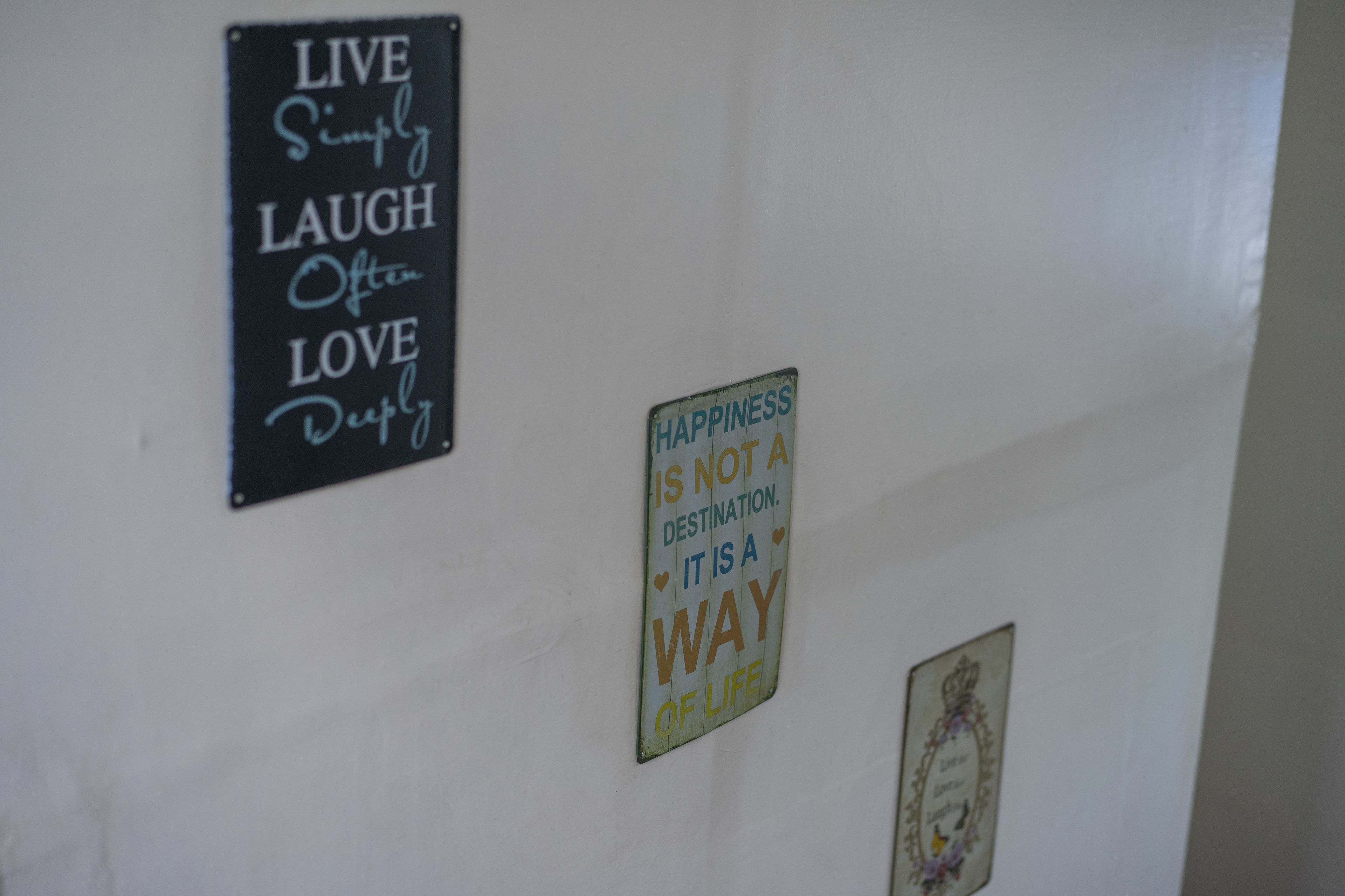 Een muur met drie motiverende borden: 'LEEF Eenvoudig LACH Vaak HOU Diep', 'GELUK IS GEEN BESTEMMING. HET IS EEN WIJZE VAN LEVEN', en een ingelijst foto.