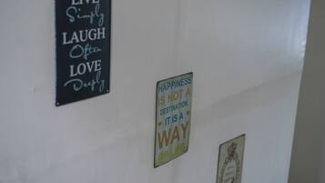 Een muur met drie motiverende borden: 'LEEF Eenvoudig LACH Vaak HOU Diep', 'GELUK IS GEEN BESTEMMING. HET IS EEN WIJZE VAN LEVEN', en een ingelijst foto.