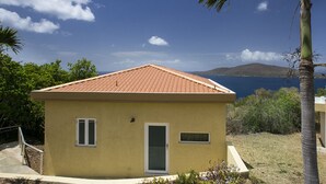 Il s’agit d’un petit bâtiment d’un seul étage, doté d’un toit recouvert de tuiles rouges, d’une porte et de deux fenêtres. Il est entouré de verdure et offre une vue sur la mer et les collines qui se dessinent à l’arrière-plan.