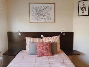 Cama bem arrumada com roupa de cama listrada, cabeceira escura e duas luminárias de apoio.