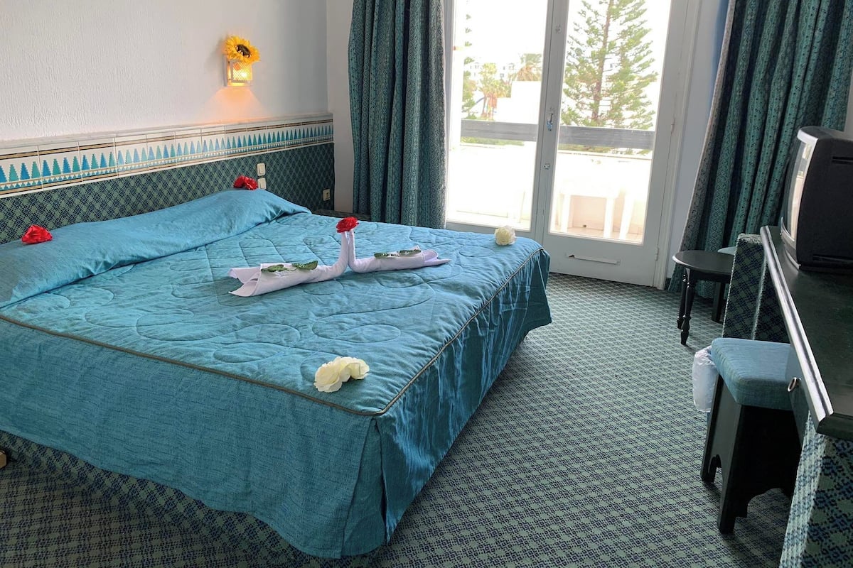 A hotel room with a bed, a desk, a chair, and a view of the outdoors.