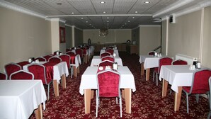 Une salle de conférence avec des rangées de tables et de chaises, un sol recouvert de moquette et un plafond orné de motifs.
