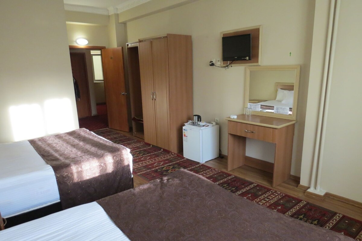 A hotel room with two beds, a desk with a mirror, a television, and a small refrigerator.