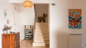 A staircase with a wooden finish, a hanging light fixture, and a wall-mounted radiator. - Eco Soul Ericeira Guesthouse (Mafra)