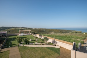 Un espacio al aire libre con jardines, una terraza de madera, un pérgola y vistas al mar.