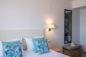 Una cama bien hecha con dos almohadas, una lámpara de noche, una mesita de noche de madera y un espejo en la pared.