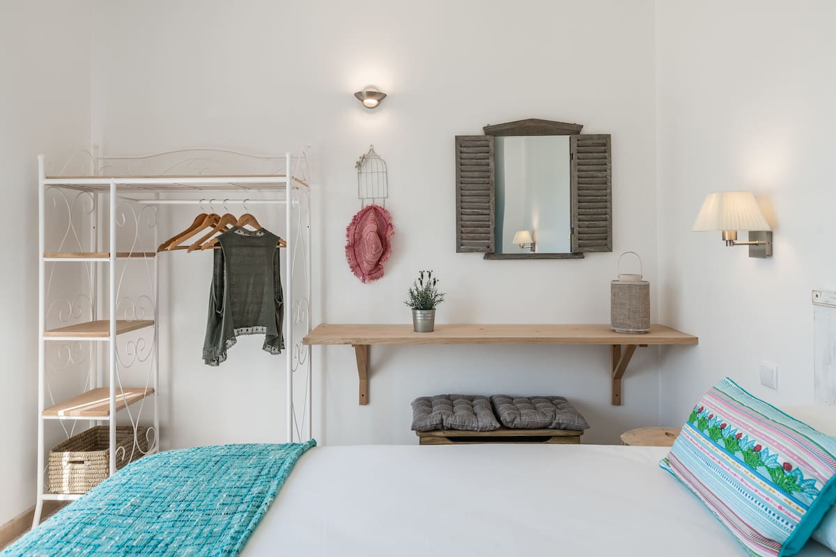 A bedroom with a bed, a wardrobe, a mirror, a shelf with a plant, and a bedside lamp.