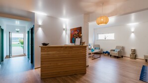 A reception area with a wooden desk, a painting on the wall, and a window providing natural light. - Eco Soul Ericeira Guesthouse (Mafra)