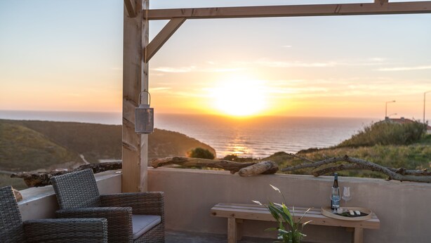 A balcony with wicker furniture, a wooden bench, and a table with a potted plant. - Eco Soul Ericeira Guesthouse (Mafra)