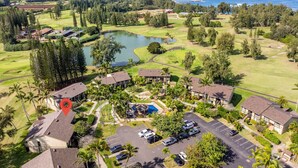 An aerial view of a golf course with a swimming pool, multiple buildings, and a parking area. - Spacious Townhome with Golf Course Views (Kahuku)