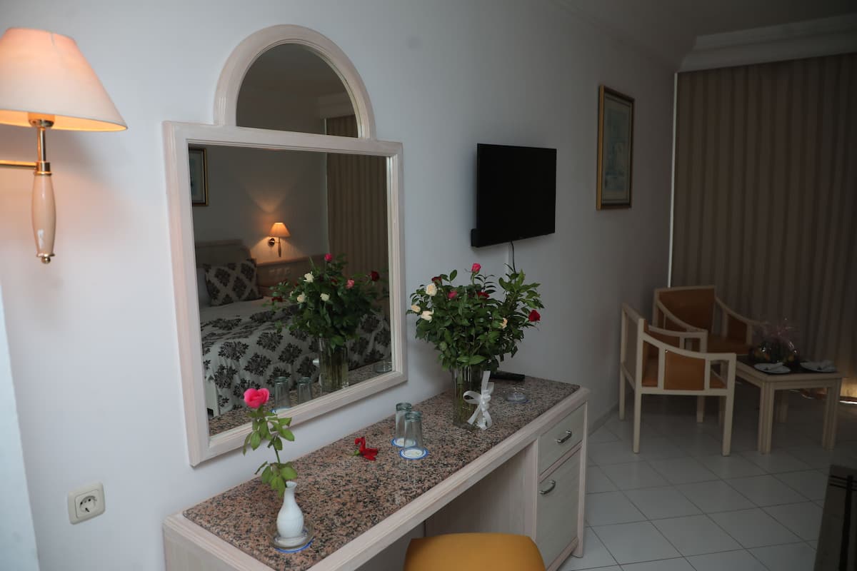 A hotel room with a vanity, a mirror, a television, a dining area with chairs, and a window with curtains.