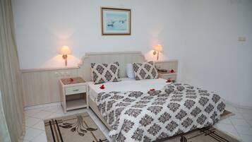 A bedroom with a bed, two bedside tables, a nightstand, a lamp, a framed picture on the wall, and a patterned rug.