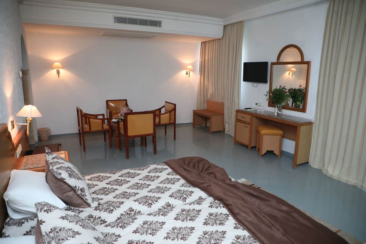 A hotel room with a bed, desk, chairs, and a TV.