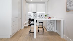 A modern kitchen with white cabinetry, a marble backsplash, and two black bar stools. - VI Castle Lane (London)