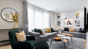 A modern living room with a grey sofa, green armchairs, and a coffee table with oranges. - VI Castle Lane (London)