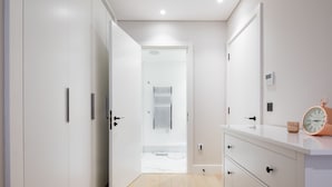 A modern hallway with white walls, a wooden floor, and a white door leading to another room. There is a white cabinet with drawers and a clock on top. - VI Castle Lane (London)
