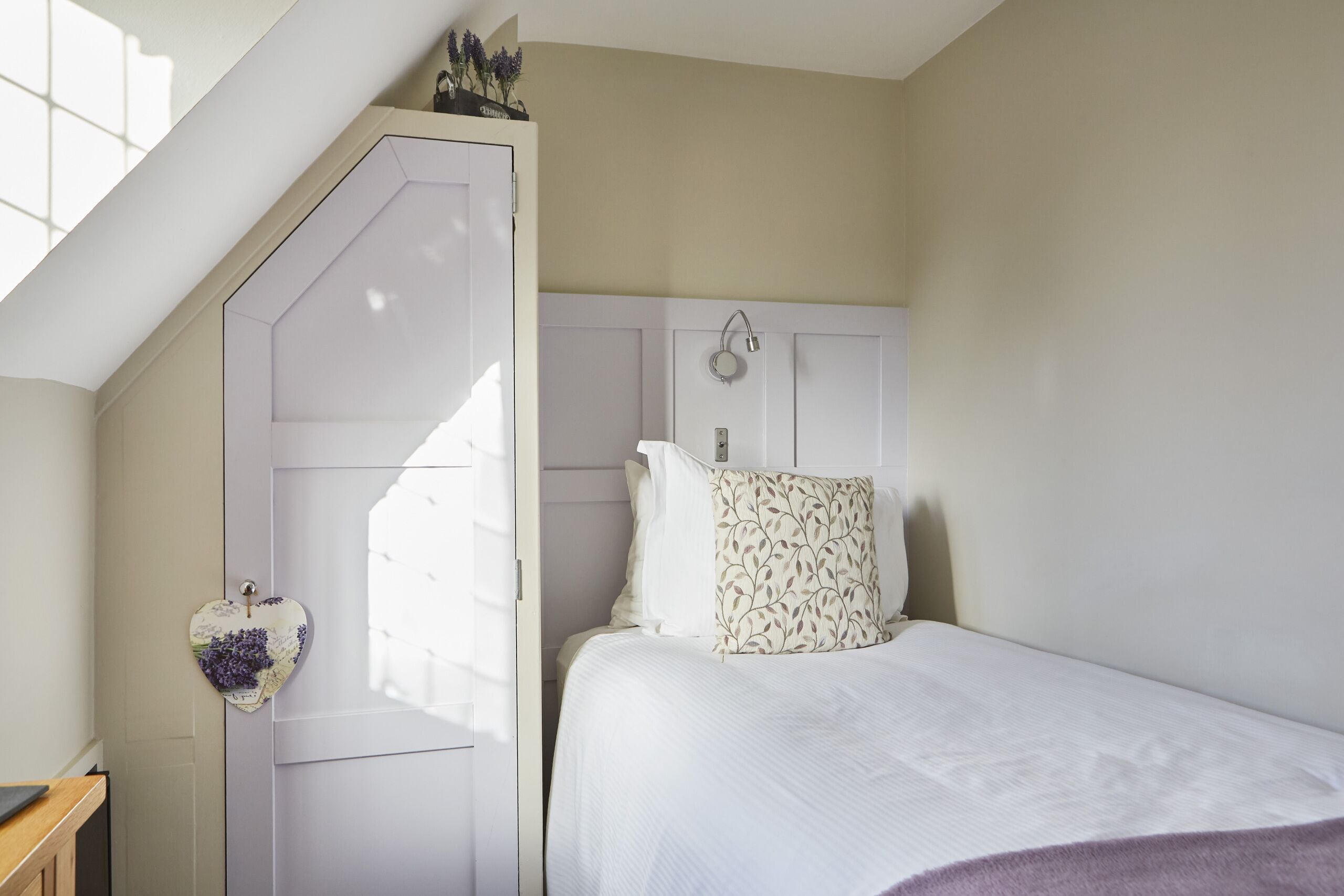 A bedroom with a white bed, a white headboard, and a door with a heart-shaped decoration.