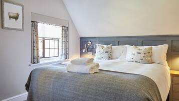 A bedroom with a large bed, a window with curtains, a headboard, and a wall-mounted lamp.
