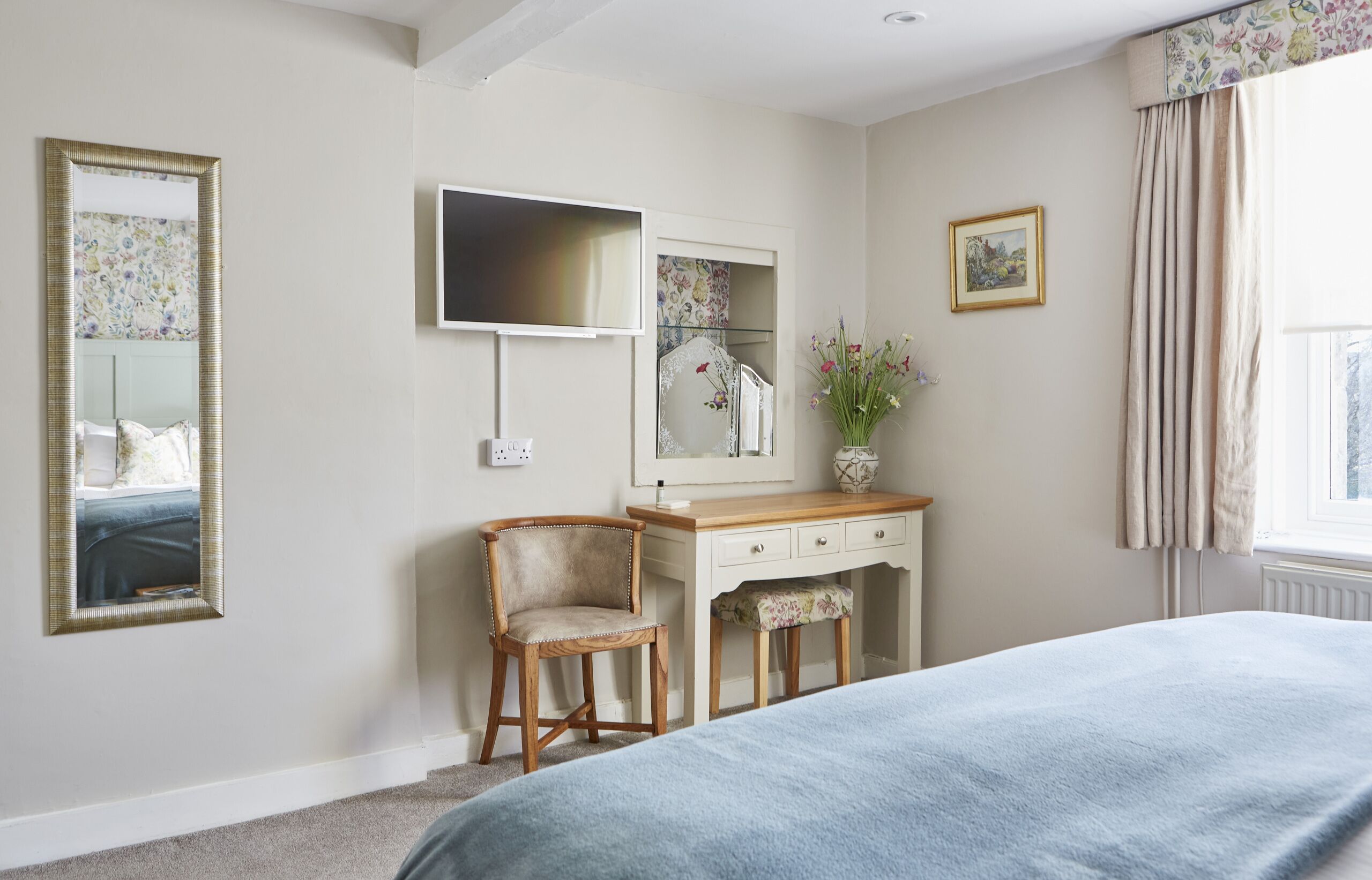 A bedroom with a bed, a wooden desk, a chair, a television, and a mirror.