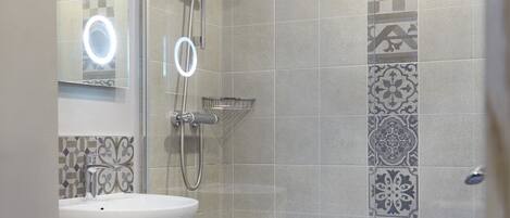 Et badeværelse med toilet, håndvask, brusebad og et gulv med mønstret flisearbejde.