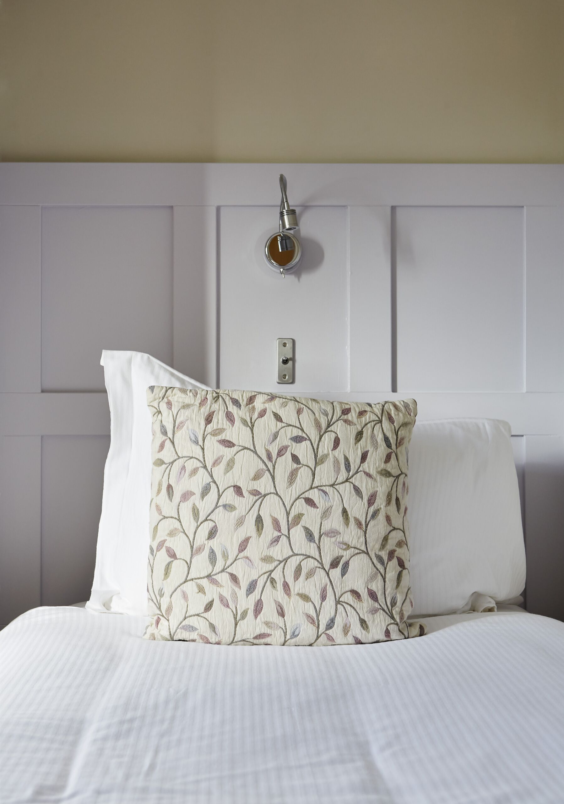 Una cama bien tendida con sábanas blancas y un cojín decorativo con estampado de hojas.
