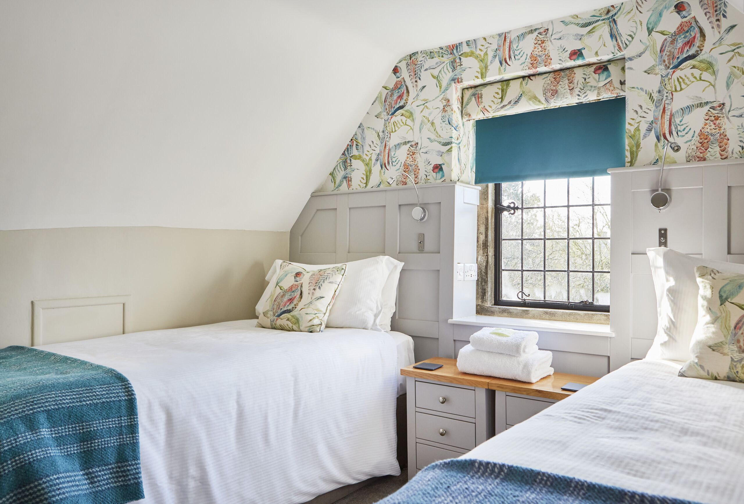 A bedroom with two beds, a window with a view, and a small bedside table with a towel and a phone.