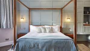A four-poster bed with a wooden frame, white bedding, and patterned pillows. There are wall-mounted light fixtures on either side of the bed. - The Old New Inn (Cheltenham)