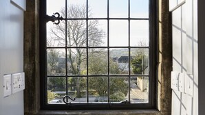 A window with a metal grid design, a stone sill, and a view of trees and buildings outside. - The Old New Inn (Cheltenham)