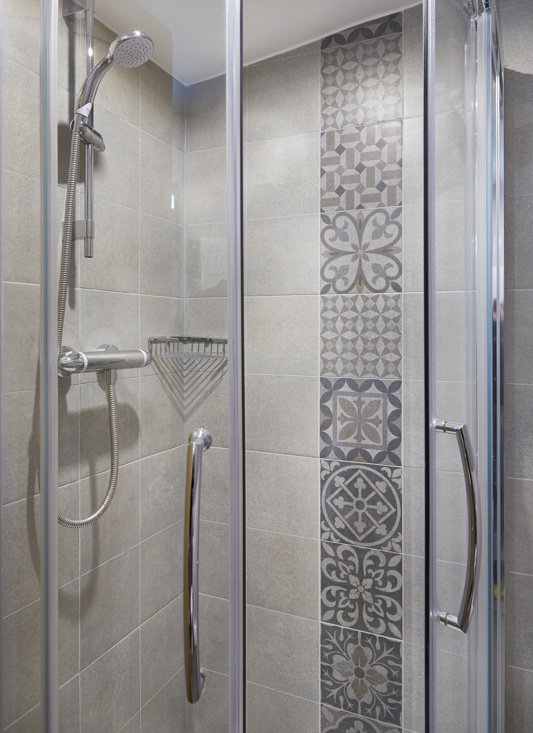 A glass-enclosed shower with a handheld showerhead and a handheld shower attachment.