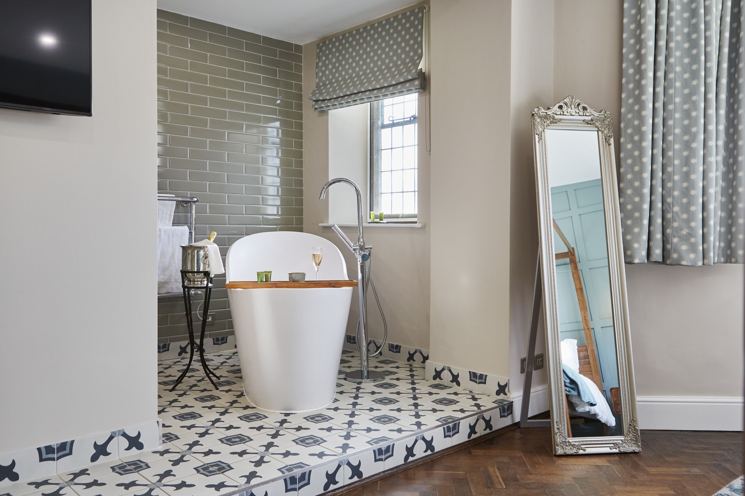 Un baño con una bañera blanca, un espejo grande y baldosas de suelo estampadas.
