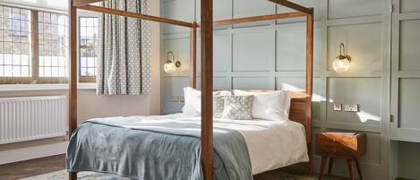 A four-poster bed with a wooden frame, a light blue bedspread, and white pillows. There are two wall-mounted lamps on either side of the bed.