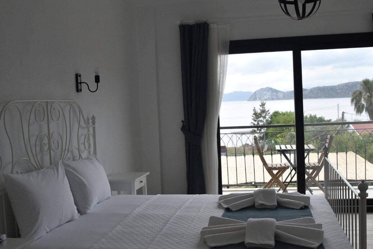 A bedroom with a bed, a nightstand, a wall-mounted lamp, and a view of the sea through a balcony.