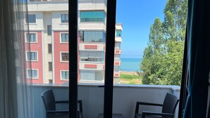 Un balcon agrémenté de deux fauteuils en osier et d’une petite table, d’où l’on peut admirer un immeuble doté de nombreux balcons et une vue sur la mer.