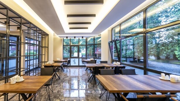 Un espace de restauration intérieur moderne, doté de grandes fenêtres, de tables en bois et de chaises noires.
