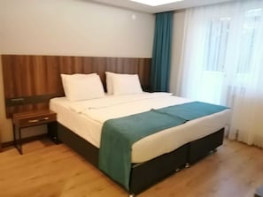A hotel room with a wooden headboard, a bed with white bedding, a teal throw blanket, and a nightstand. - Ferah Suites (Akçaabat)