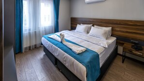 Une chambre d’hôtel avec un lit en bois, du linge de lit blanc, un coussin bleu décoratif, une table de chevet en bois et un appareil de climatisation.