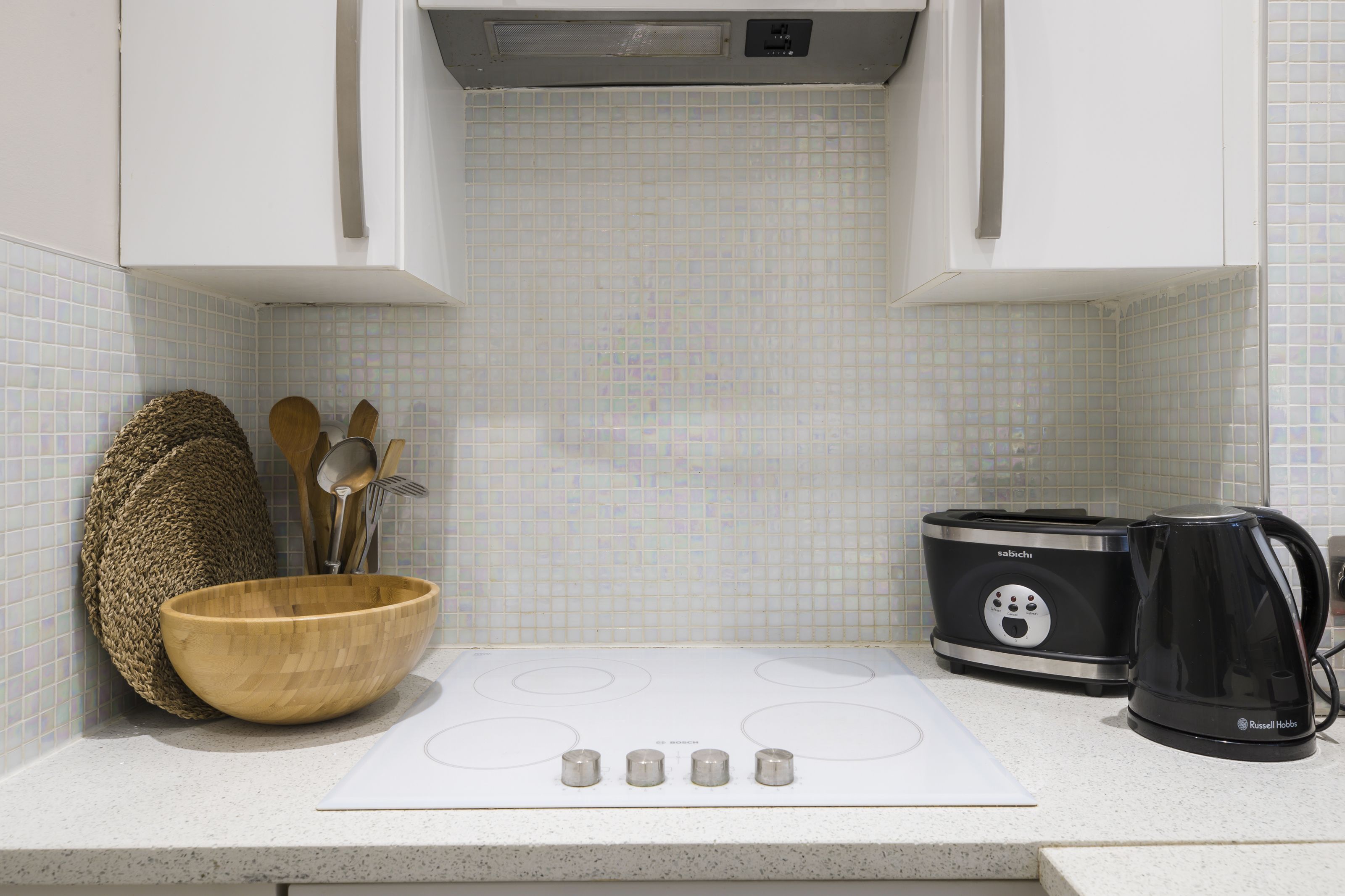 A kitchen with a white stove, a wooden bowl, a kettle, and a toaster.