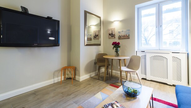 A modern living room with a flat-screen TV mounted on the wall, a dining area with a small round table and chairs, and a large window providing a view of the outdoors. - Westbourne Gardens by Lime Street (London)