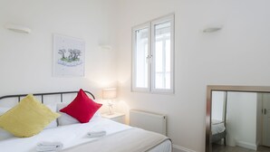 A neatly made bed with white linens and two pillows, a bedside lamp, a radiator, a window with blinds, and a mirror on the wall. - Westbourne Gardens by Lime Street (London)