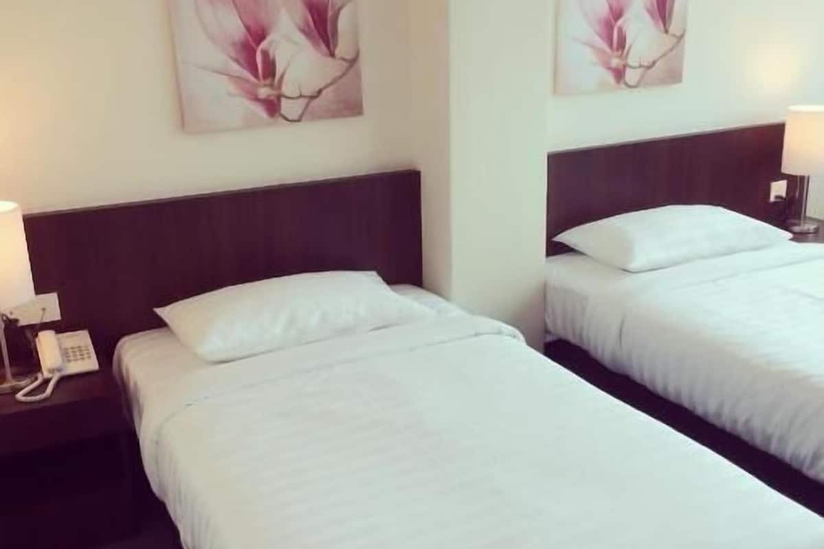 A hotel room with two beds, a nightstand with a phone, and wall art.