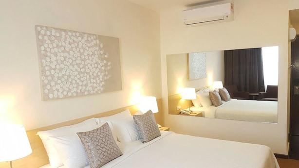 A hotel room with a large bed, two bedside lamps, a wall-mounted air conditioner, and a large mirror reflecting the room. - The View Hotel (Segamat)